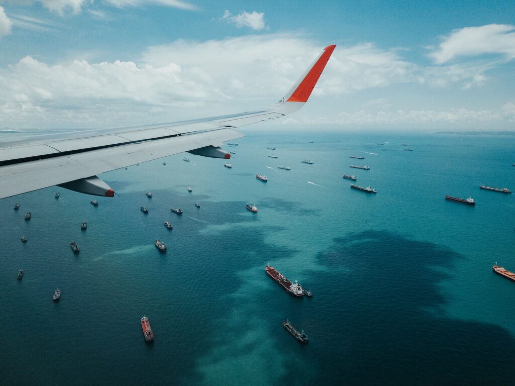 A plane that's shipping goods internationally flying over the sea with ships in sight